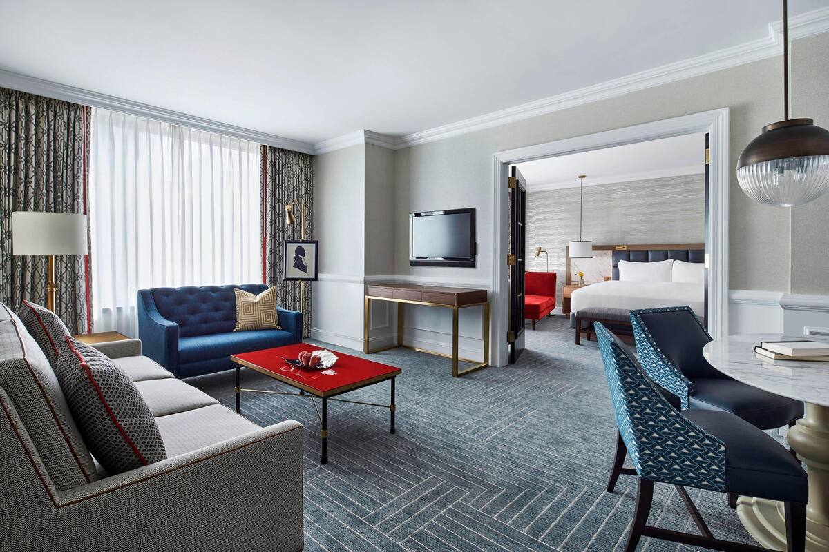 A hotel room with a sofa, a red coffee table, a TV, a desk, and a bed.