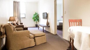 A hotel room with a sofa, ottoman, TV, and a dining table. - The Richmond Hotel - Adelaide (Adelaide)