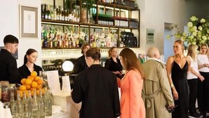 A bar area with a counter, shelves of bottles, and a group of people standing and conversing. - The Richmond Hotel - Adelaide (Adelaide)