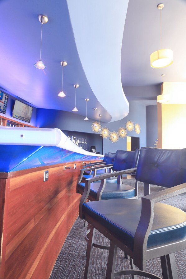A modern bar area with a curved wooden counter, multiple seating options, and pendant lighting.