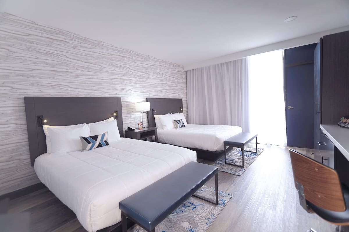 A hotel room with two beds, a bench, a desk, and a TV.