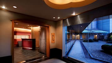 A modern hotel lobby with a reception desk, a large window overlooking a garden, and a traditional Japanese sign.