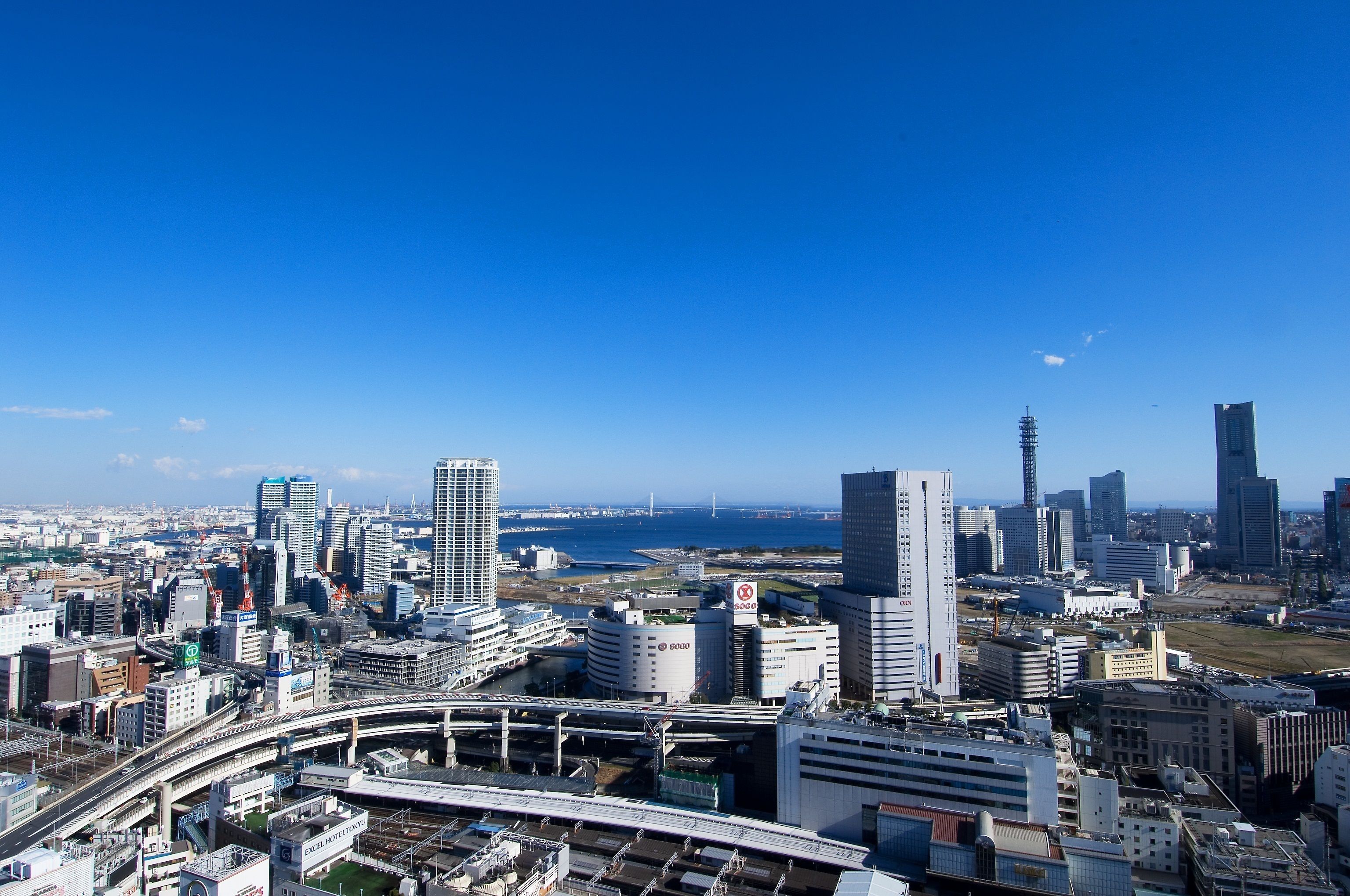 Une vue urbaine avec de hauts immeubles, un pont et une étendue d’eau au loin.