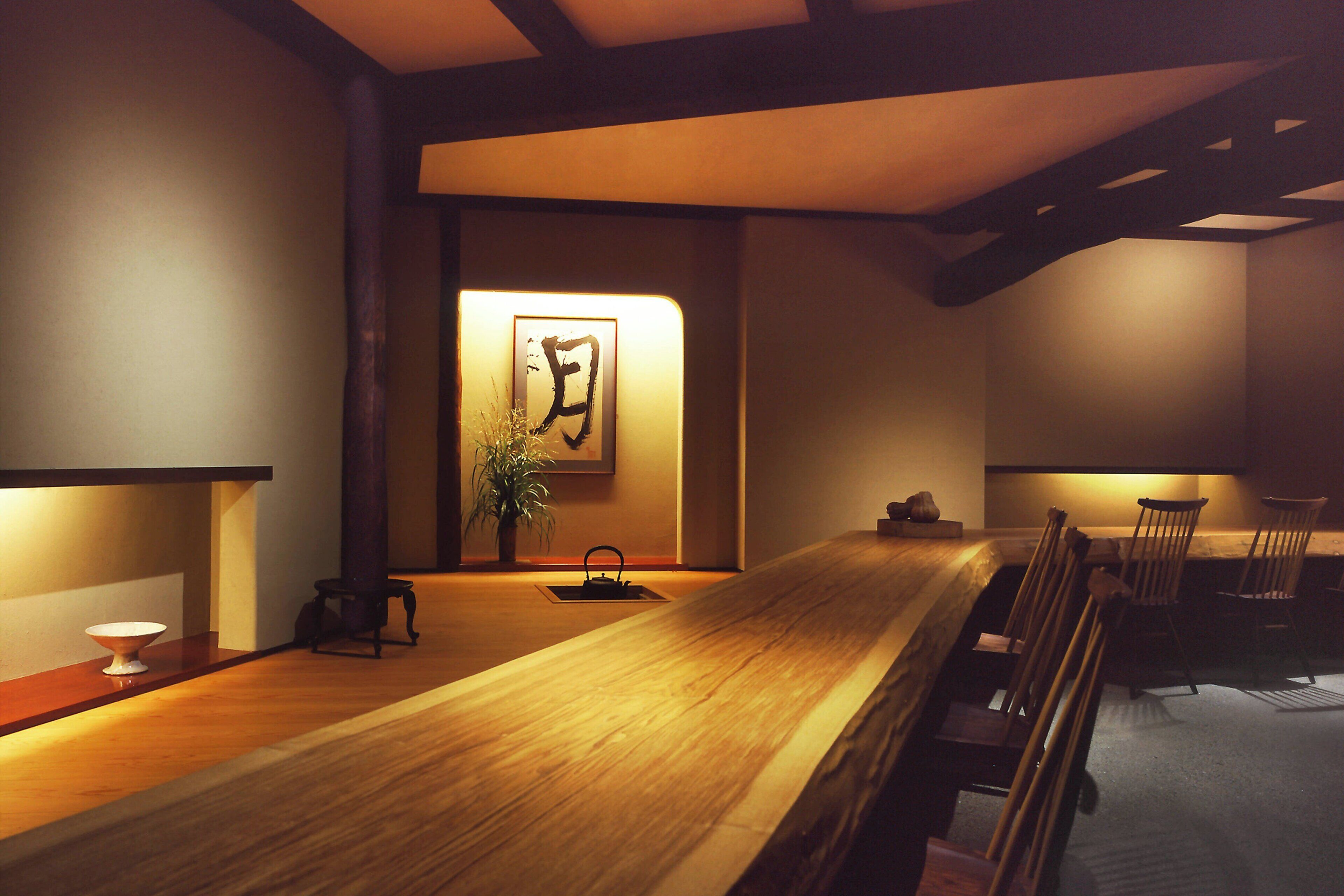 Una habitación tradicional japonesa con una mesa de madera, sillas, suelo de esteras de tatami, un hervidor de agua y una obra de caligrafía enmarcada en la pared.