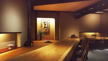 Una habitación tradicional japonesa con una mesa de madera, sillas, suelo de esteras de tatami, un hervidor de agua y una obra de caligrafía enmarcada en la pared.