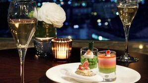 A table with two glasses of wine, a candle, and a dessert plate with three desserts.