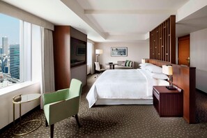 A hotel room with a large bed, a green chair, a small table, a nightstand, a lamp, a painting on the wall, and a view of the city through the window. - Yokohama Bay Sheraton Hotel & Towers (Yokohama)