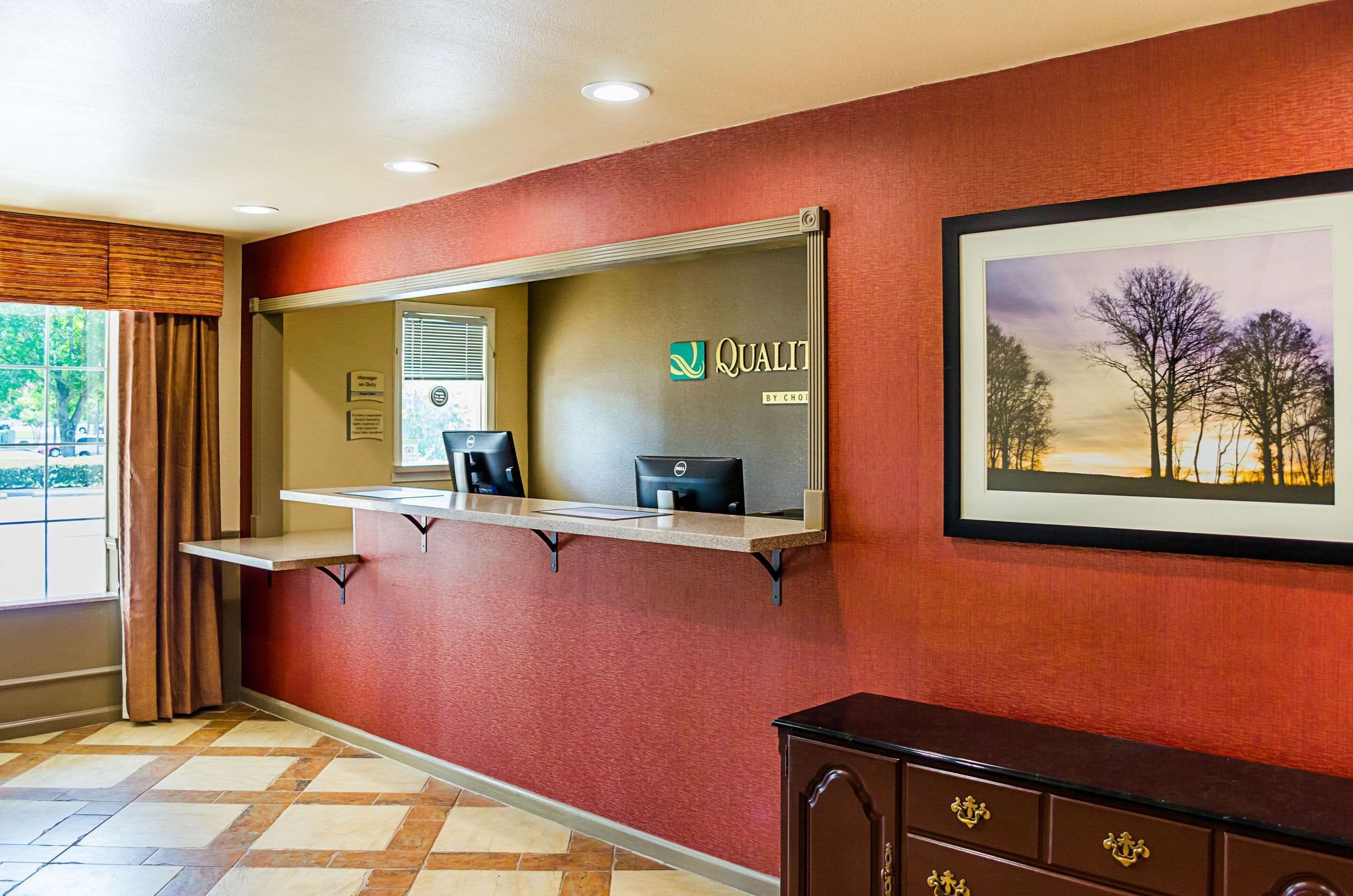 A reception area with a desk, a framed picture on the wall, and a window with curtains.
