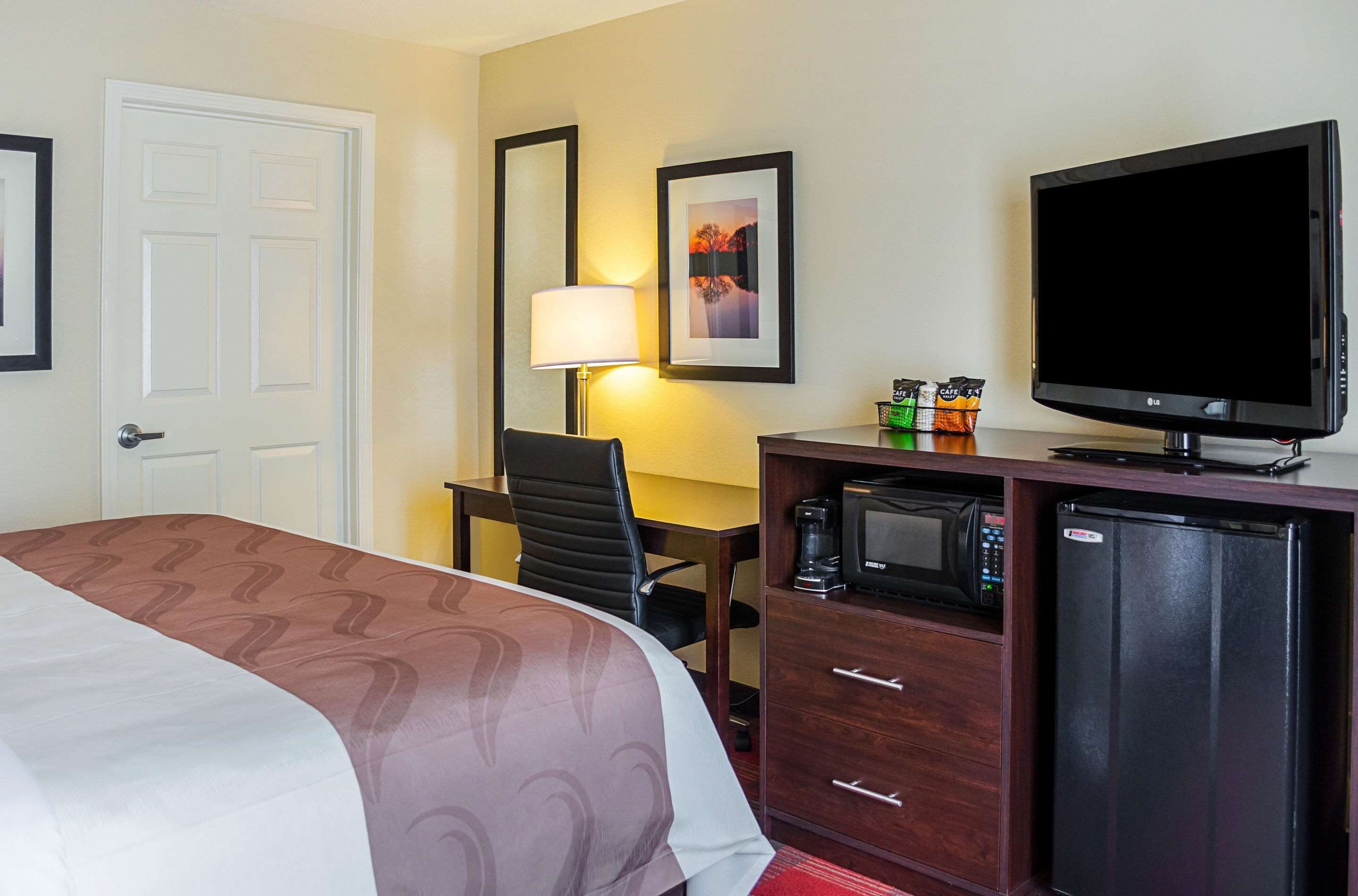 Una habitación de hotel con una cama, un escritorio con silla, televisión, microondas y refrigerador.
