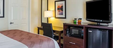 Una habitación de hotel con una cama, un escritorio con silla, televisión, microondas y refrigerador.