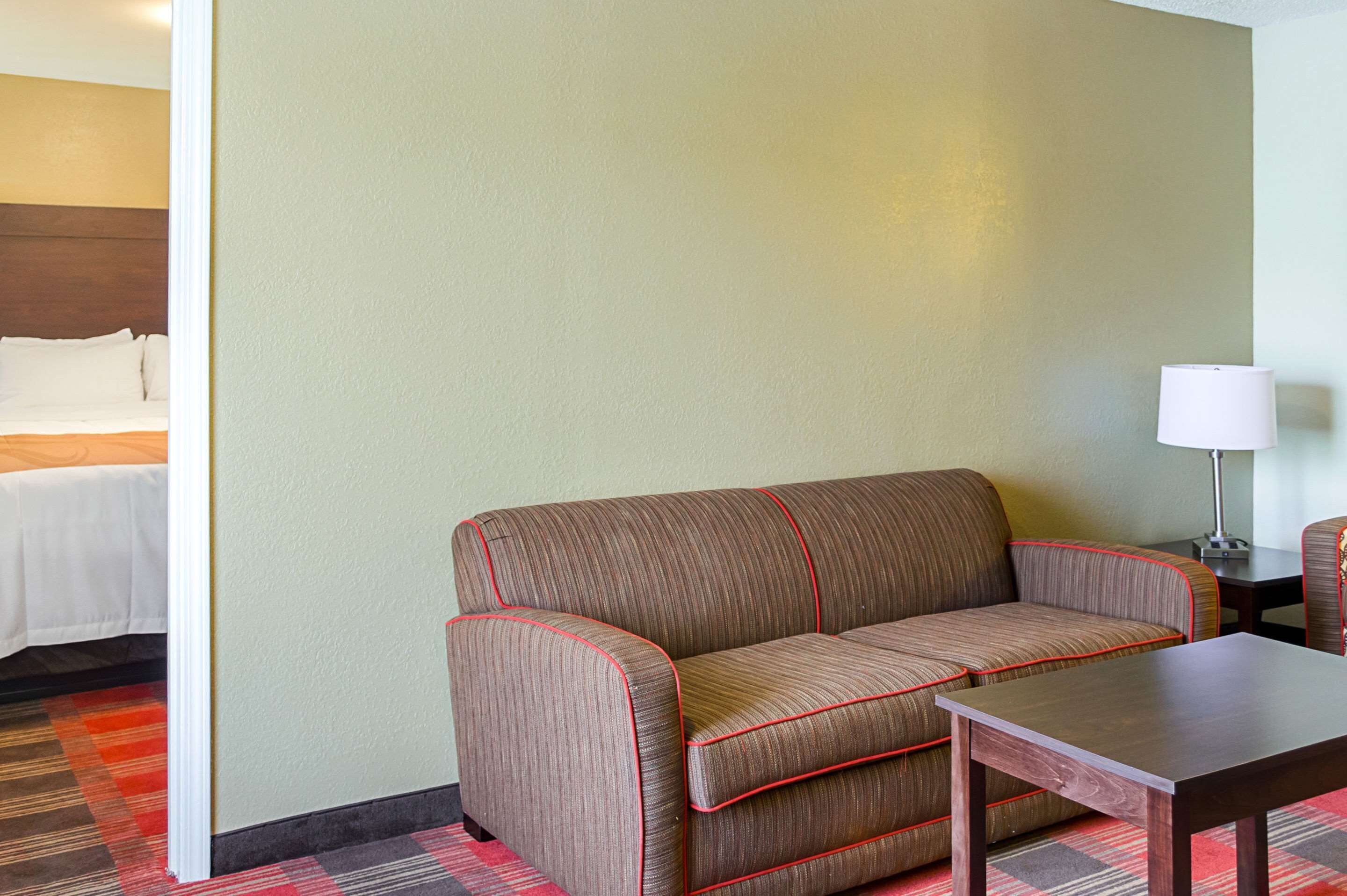 Ein Hotelzimmer mit einer Couch, einem kleinen Tisch, einer Lampe und einem Bett mit weißer Bettdecke.