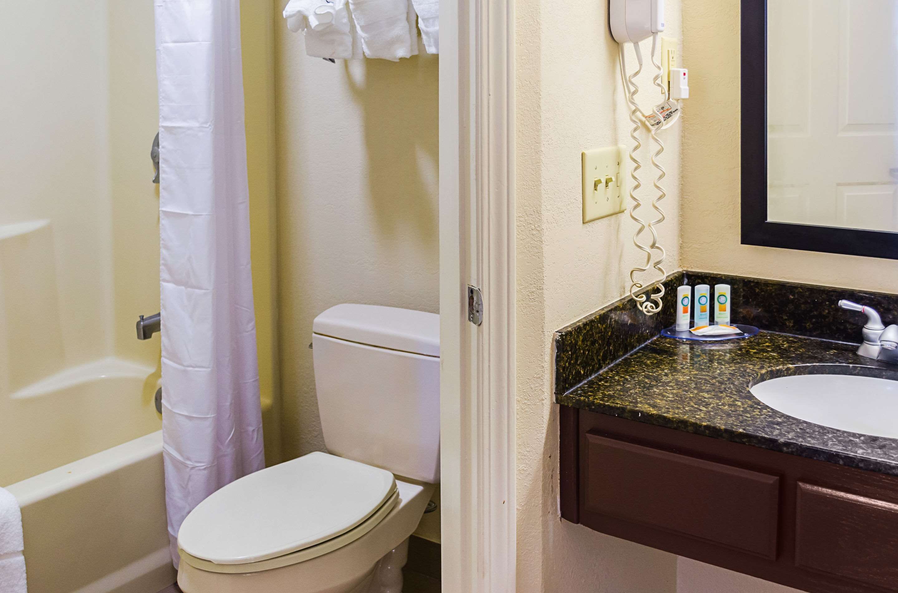A bathroom with a toilet, a shower curtain, a sink with a mirror, and toiletries.