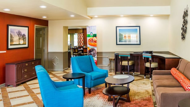 A hotel lobby with blue armchairs, a brown sofa, a coffee table, and a dining area with chairs and a table. - Quality Inn Vicksburg (Vicksburg)