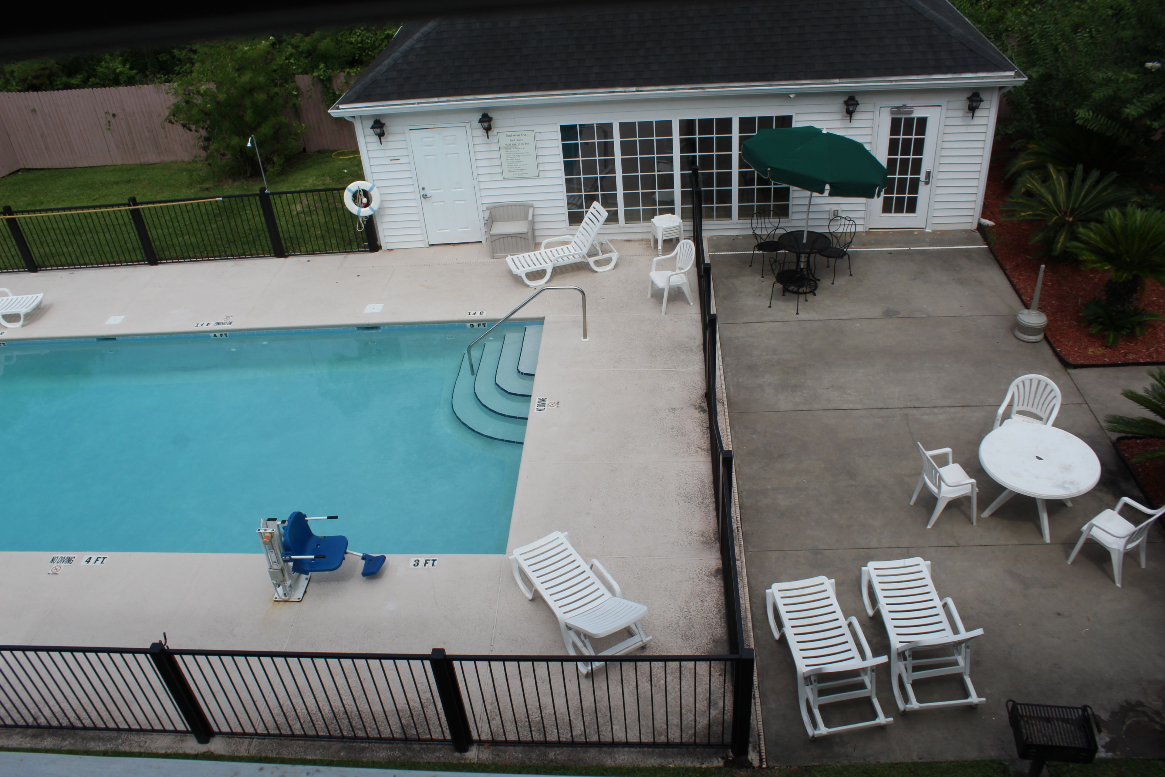A swimming pool with lounge chairs and a table, surrounded by a fence and a building with a door and windows.