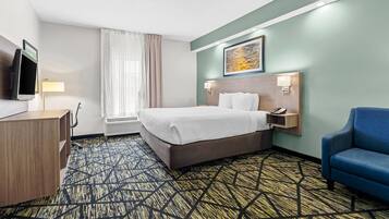 A hotel room with a bed, a desk, a chair, a TV, and a painting on the wall.