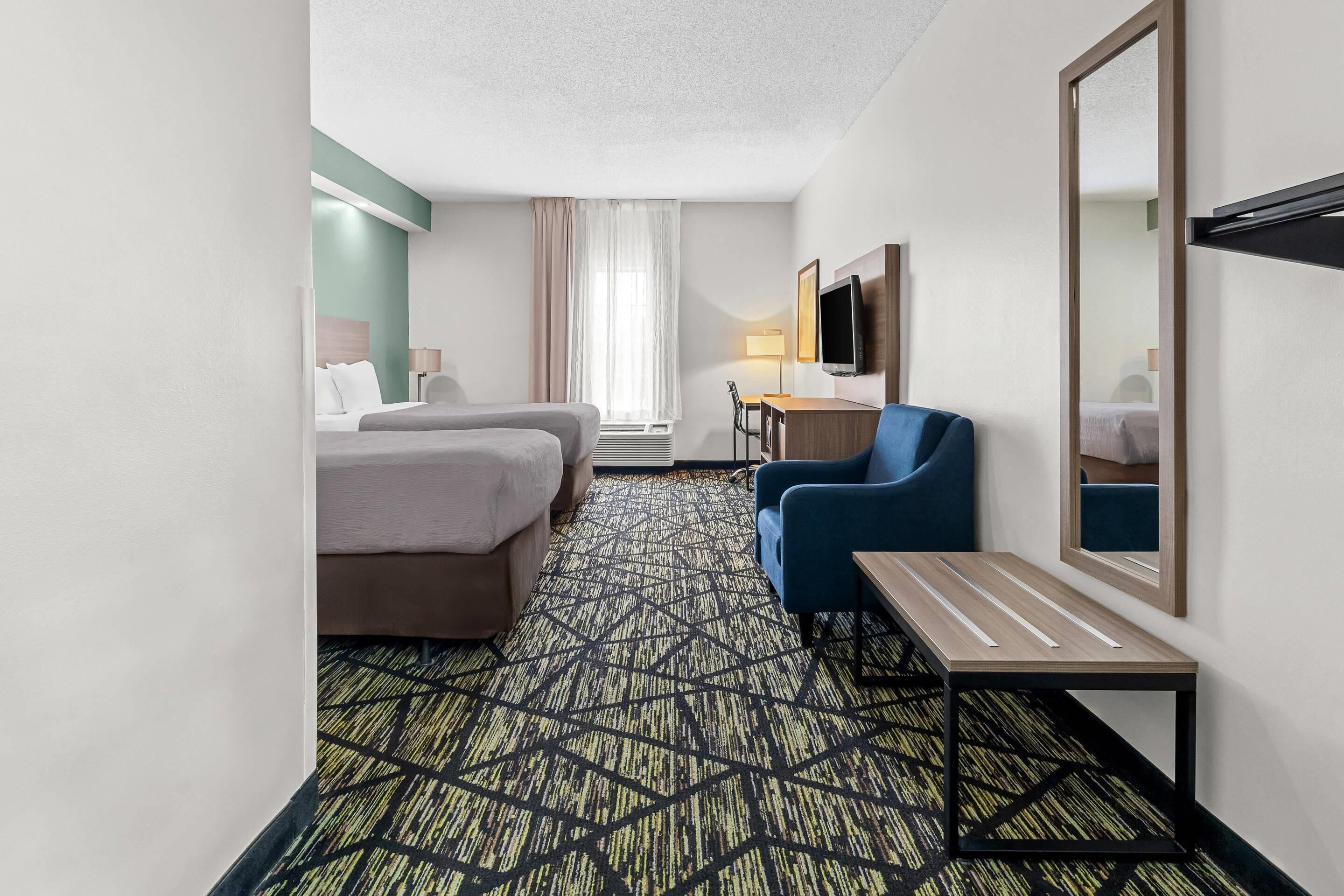 A hotel room with two beds, a desk, a chair, a TV, and a patterned carpet.