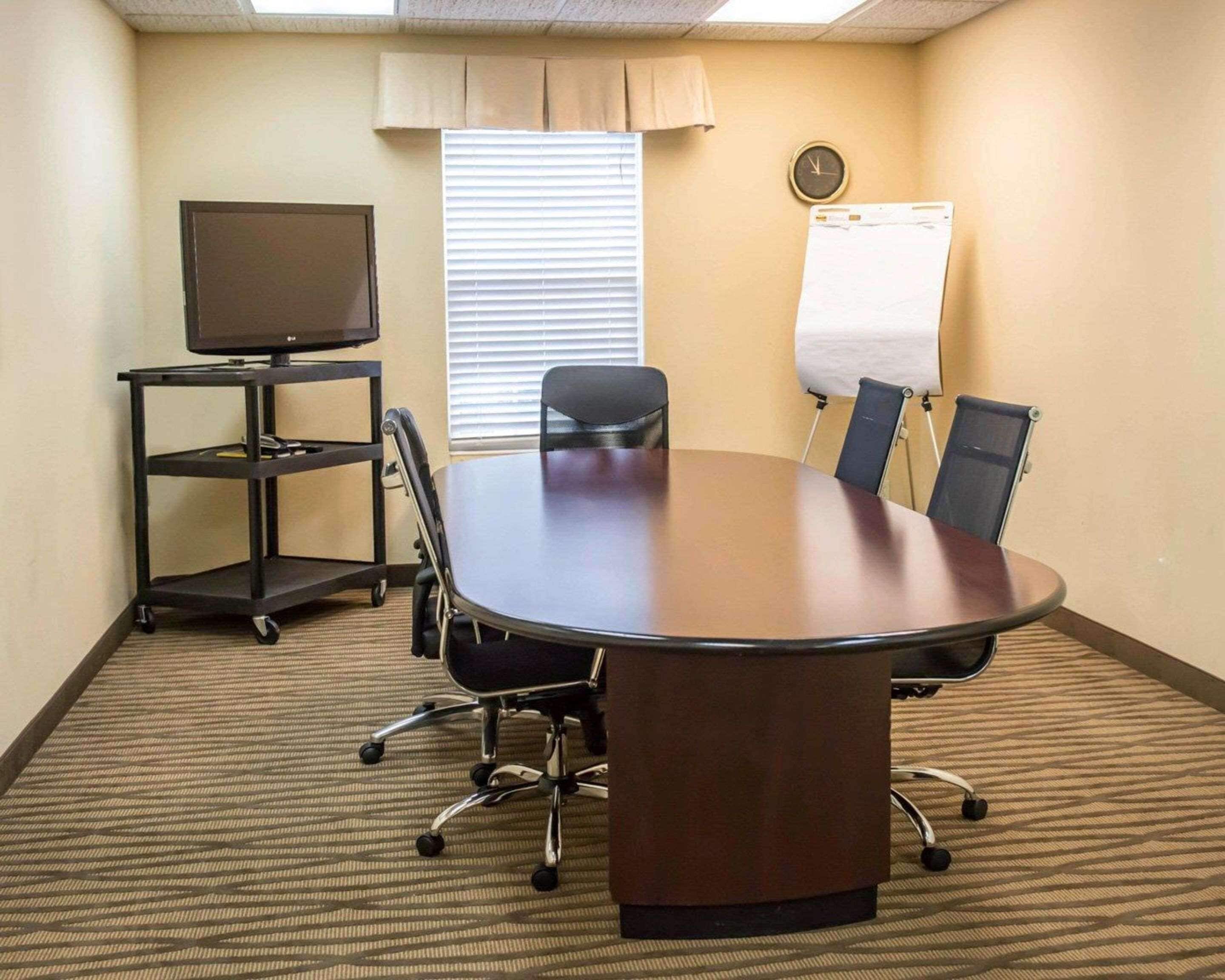A conference room with a large oval table, four chairs, a TV on a stand, a whiteboard, and a clock on the wall.