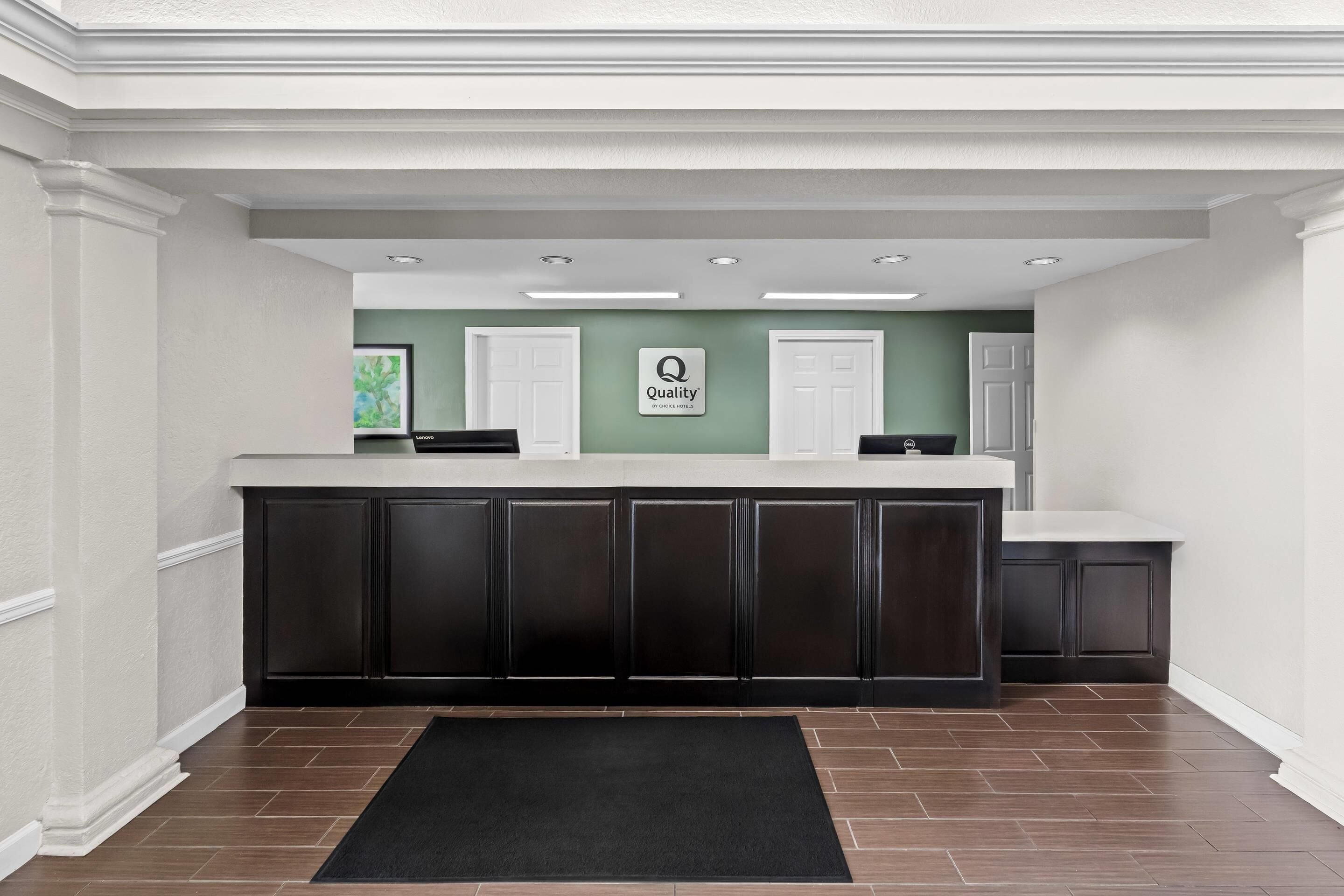A reception area with a counter, dark cabinets, a black rug, and a green wall with a 'Quality' sign.