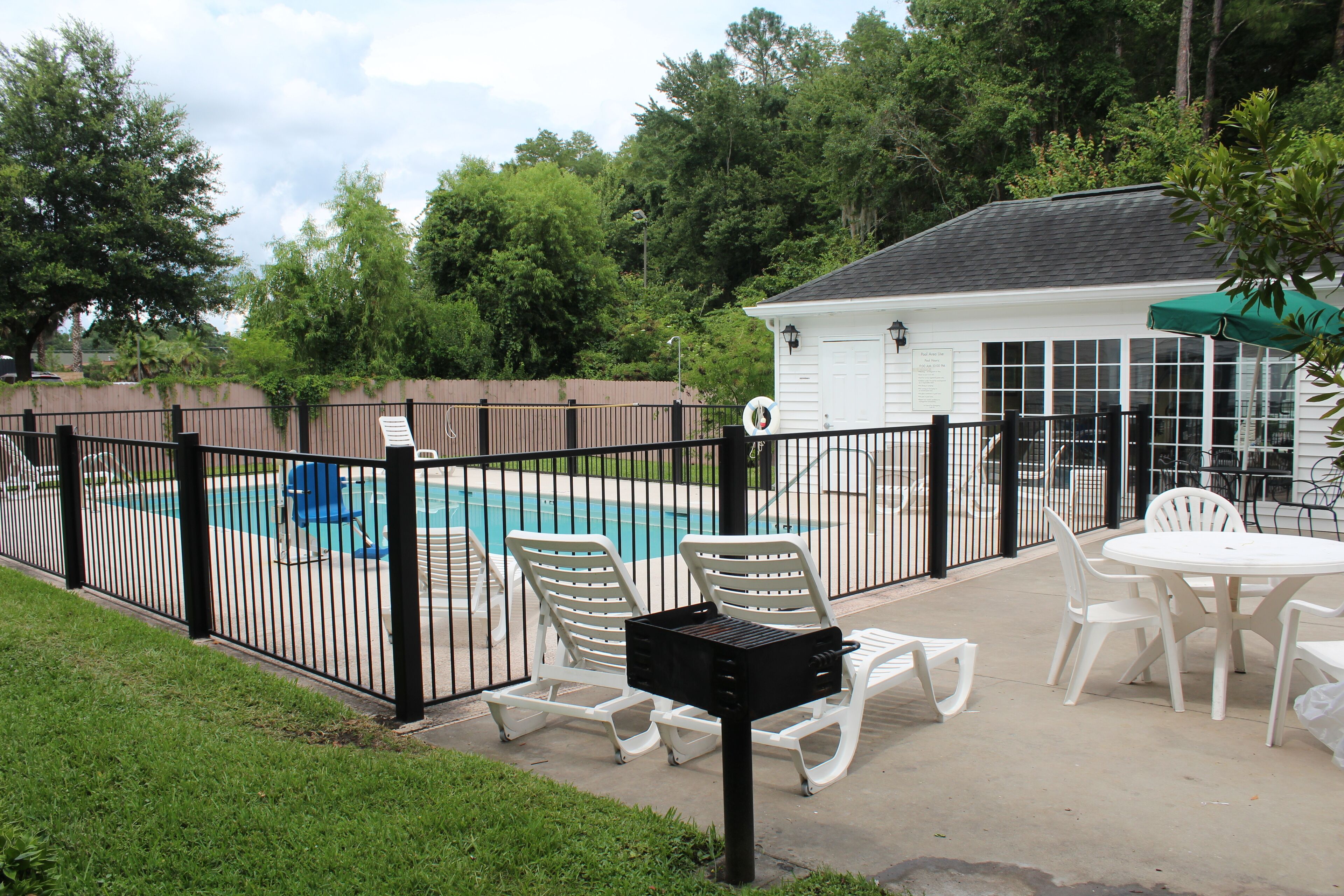 A backyard with a swimming pool, white lounge chairs, and a patio table.
