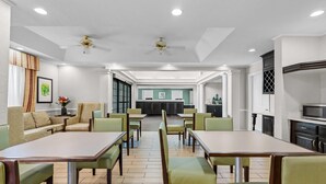 Zona de restauració d'hotel amb taules i caires, una recepció i una cuina al fons.