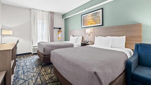 Habitació d'hotel amb dos llits, escriptori, cadira, un quadre a la paret i una catifes amb motius.