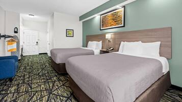 A hotel room with two beds, a blue chair, a patterned carpet, a wooden headboard, a wall-mounted phone, and a framed picture.