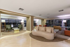 A modern living room with a curved sofa, a coffee table, and a green armchair. - Wyndham Sao Paulo Berrini (São Paulo)