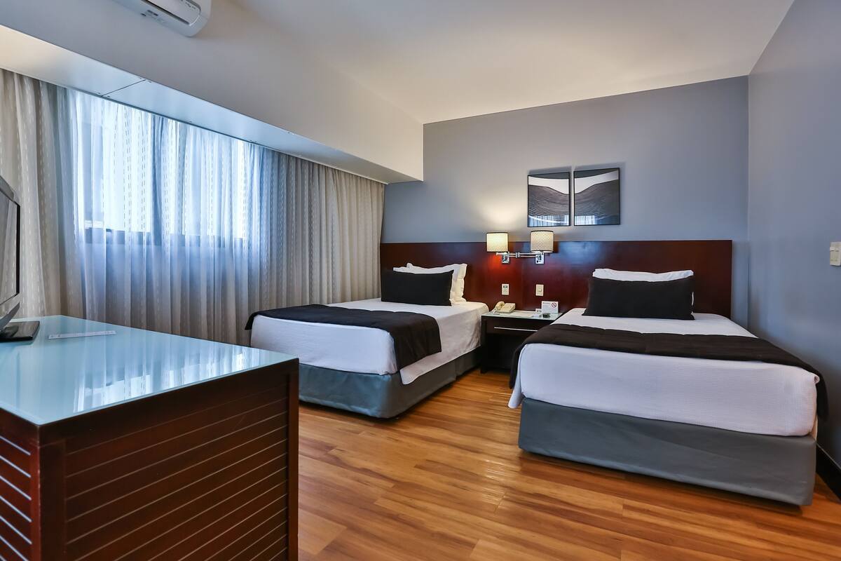 A hotel room with two beds, a desk, a telephone, and a window with curtains.