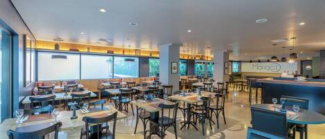 Un interior de restaurante moderno con varias mesas y sillas, una zona de bar y un ventanal que proporciona luz natural.