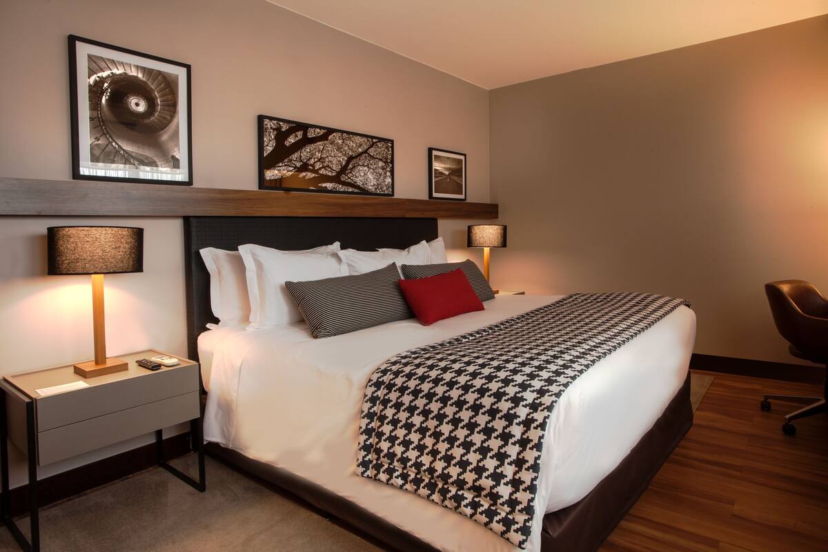 A neatly arranged hotel room with a large bed, two bedside tables with lamps, a chair, and artwork on the wall.