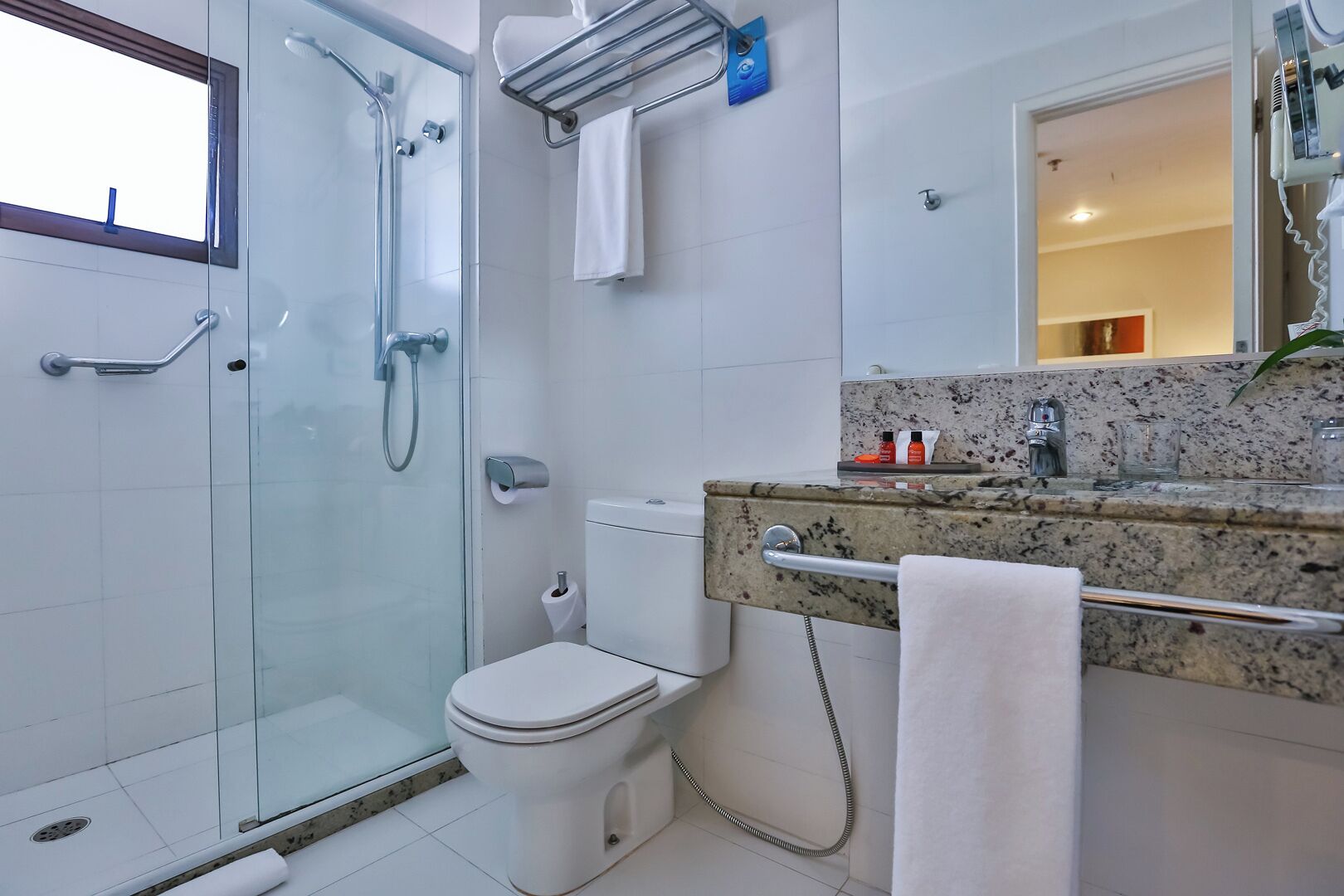 A modern bathroom with a glass shower enclosure, a toilet, and a granite countertop with a towel rack.