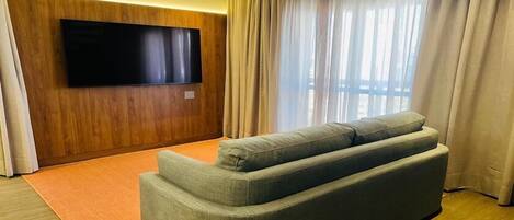 Una sala de estar moderna con un televisor de pantalla plana montado en una pared de madera, un sofá gris y un ventanal con cortinas.