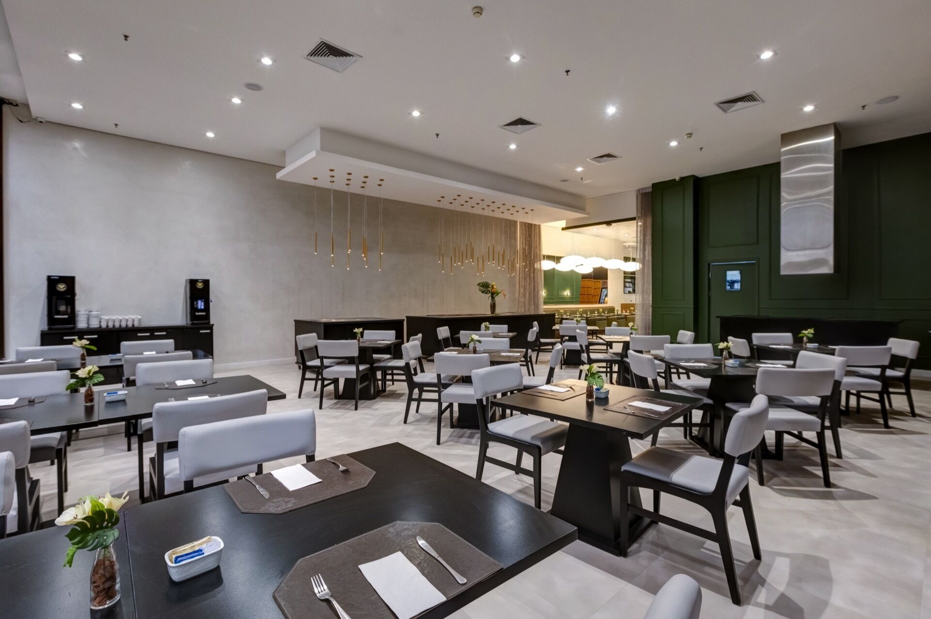 A modern conference room with multiple tables and chairs, equipped with presentation screens and a coffee machine.