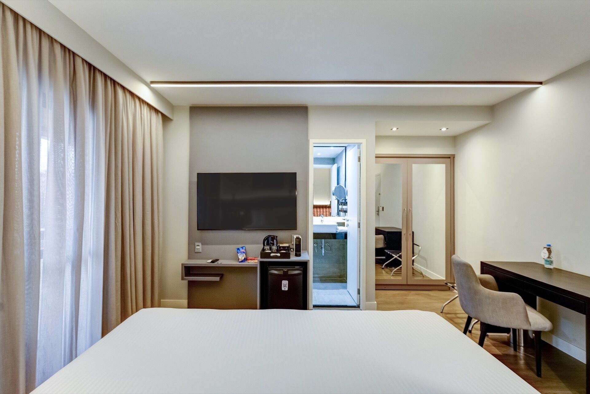 Habitación de hotel con cama, escritorio, televisión y baño visible a través de una puerta abierta.