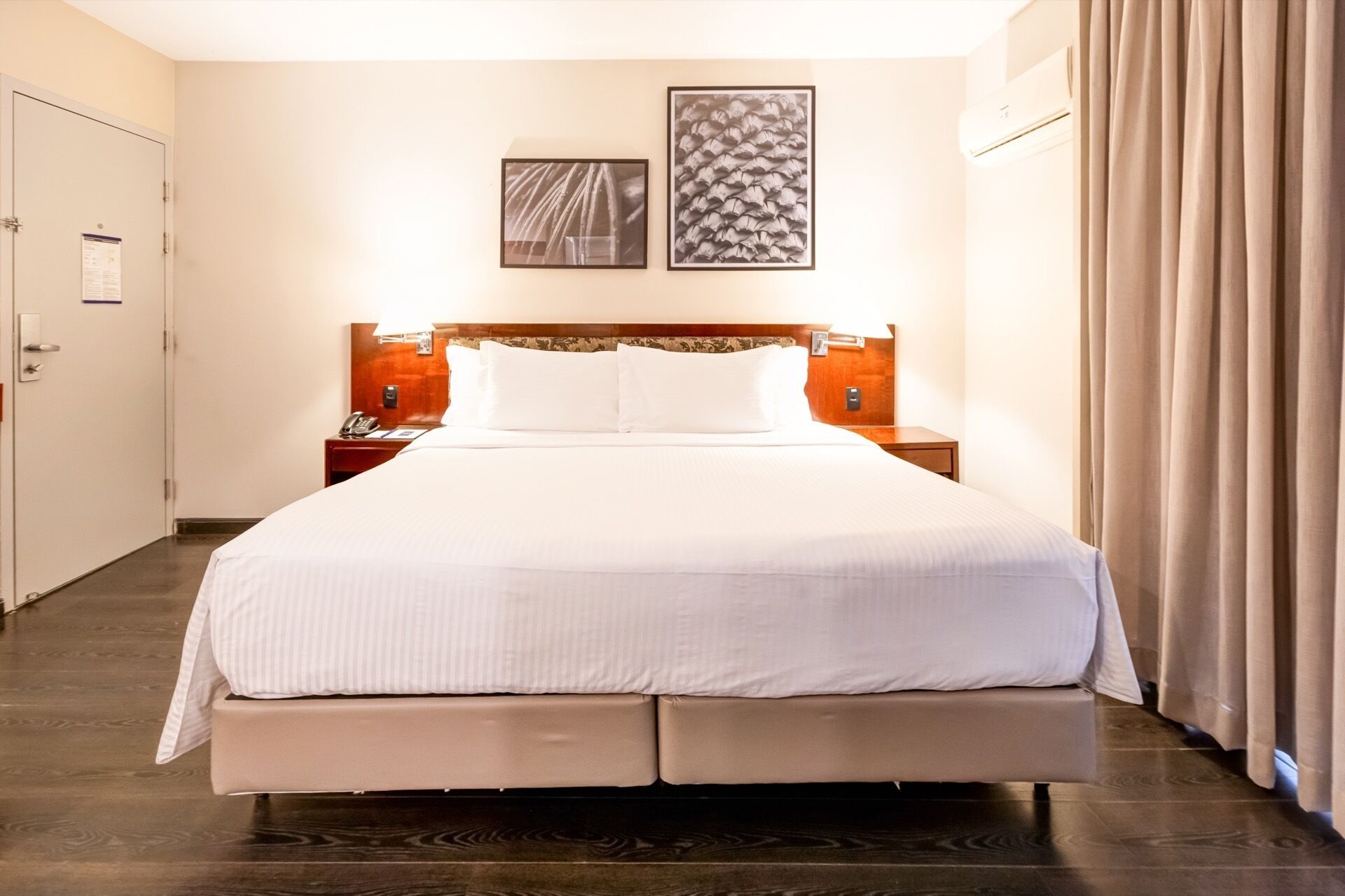 A hotel room with a large bed, two bedside tables, a headboard, and two framed pictures on the wall.
