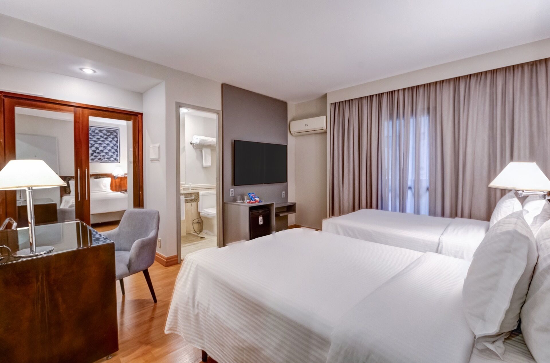 Quarto de hotel com duas camas, uma escrivaninha, uma cadeira, uma televisão e um ar condicionado.