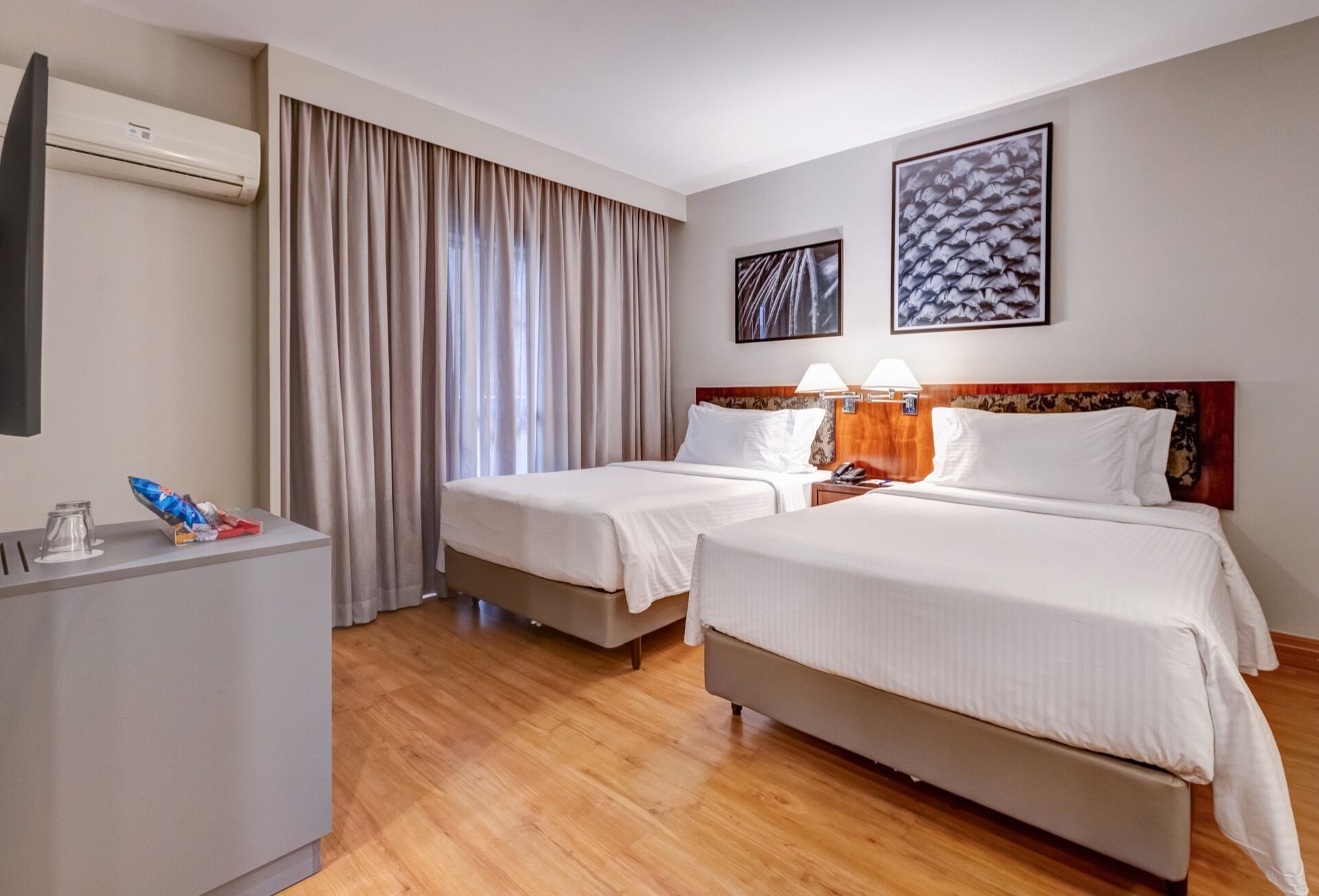 Une chambre d’hôtel avec deux lits, un bureau et une grande fenêtre avec des rideaux.