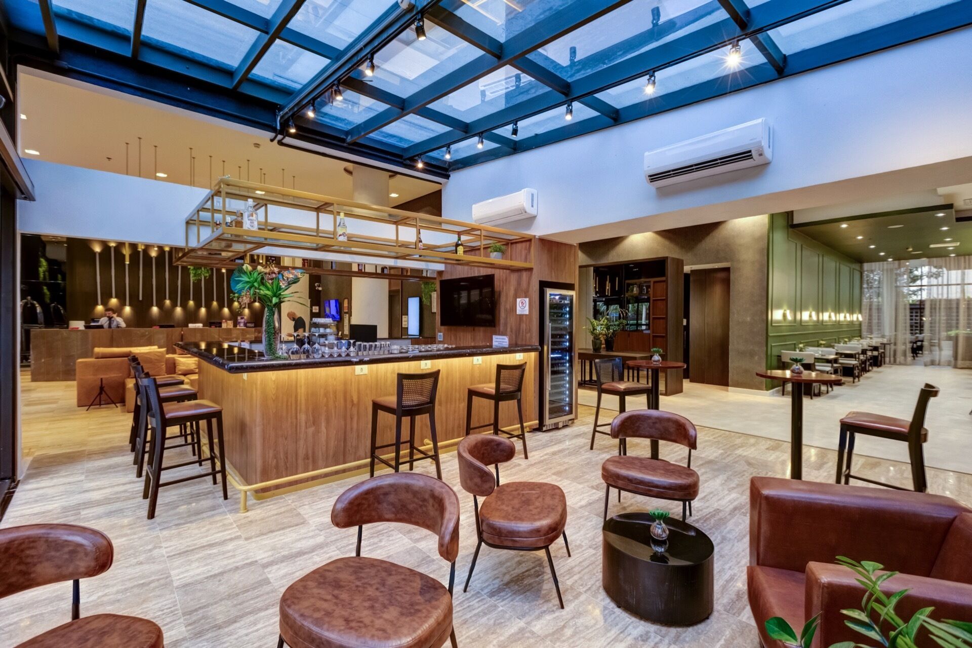 A modern bar area with a high ceiling and skylight, wooden bar counter, and leather seating.