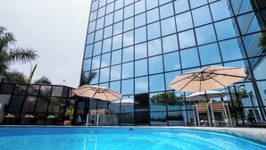 A modern building with a glass facade, a swimming pool, and outdoor umbrellas. - Melia Lima (Lima)
