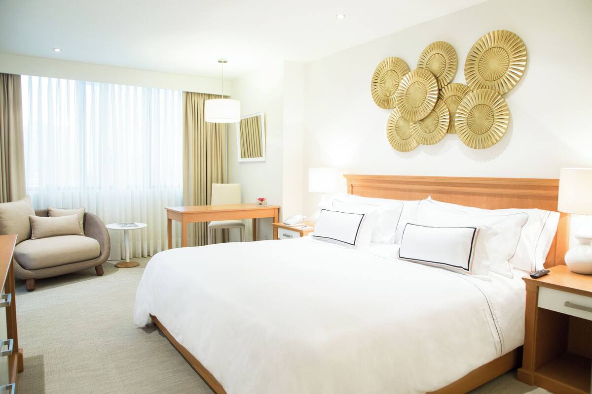 Habitación de hotel con una cama grande, un escritorio, una silla y una pared decorada con placas.