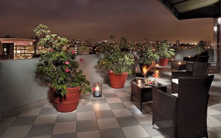 A rooftop terrace with potted plants, wicker furniture, and candles.