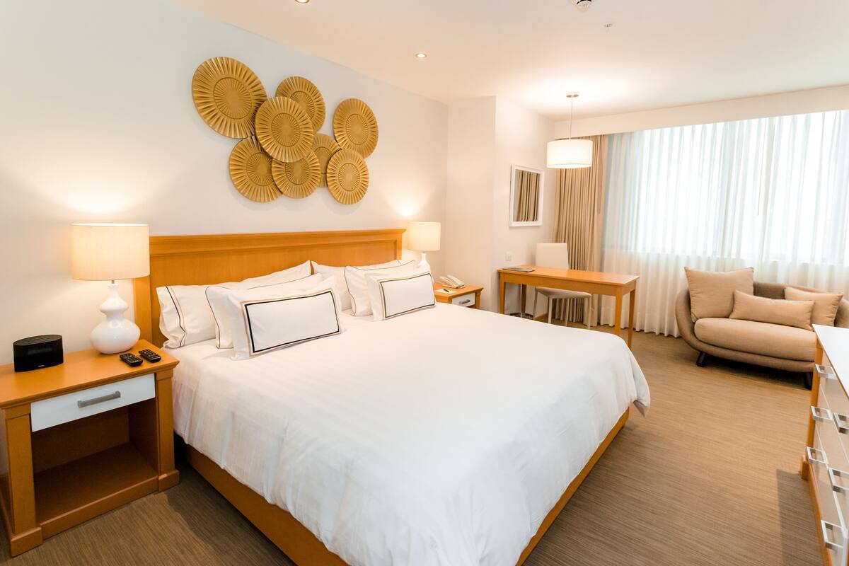 Una habitación de hotel con una cama grande, mesitas de noche, un escritorio, una silla y un sofá.