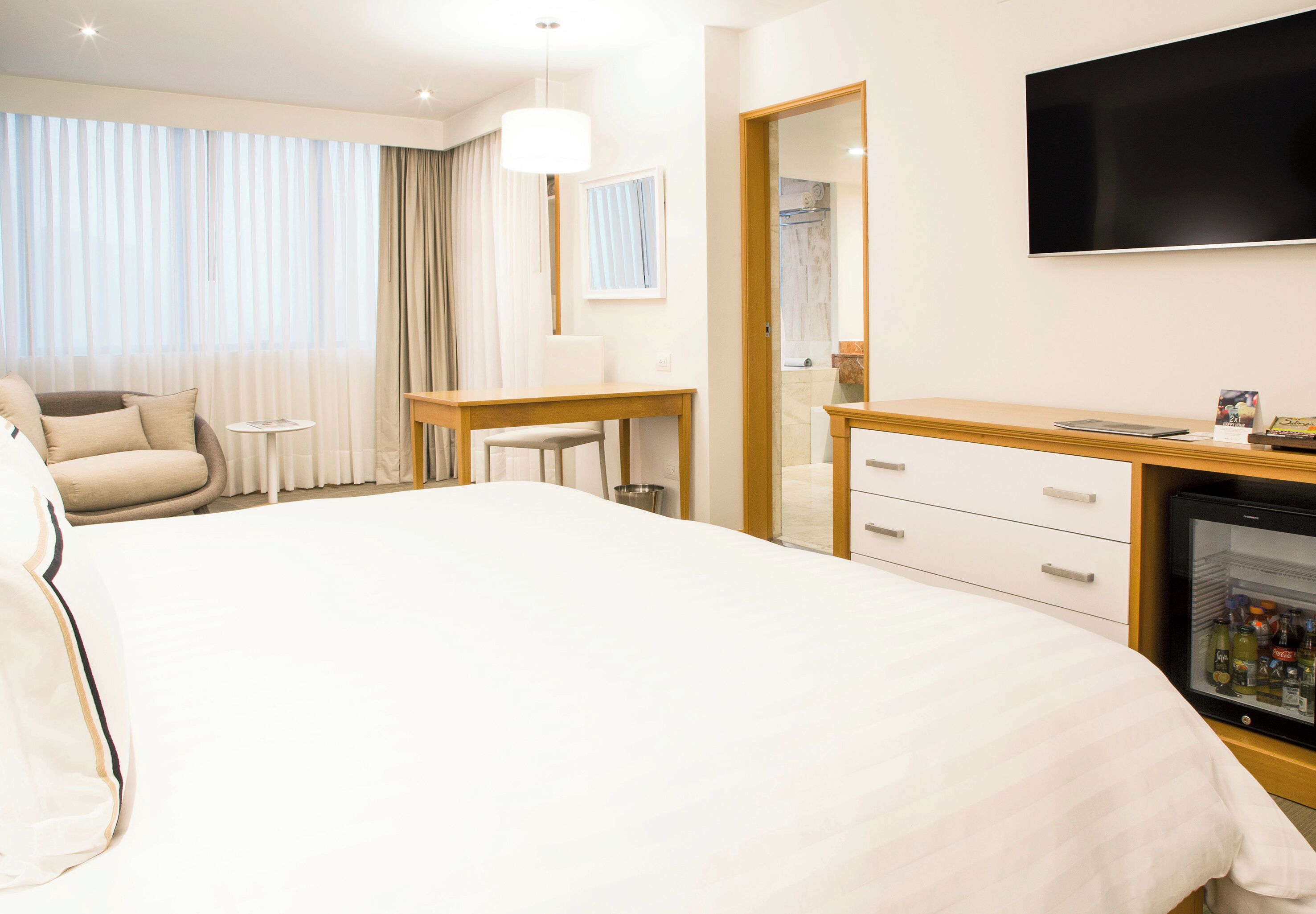 Una habitación de hotel con una cama grande, un escritorio, una silla, un televisor y un minibar.