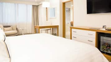 Una habitación de hotel con una cama grande, un escritorio, una silla, un televisor y un minibar.
