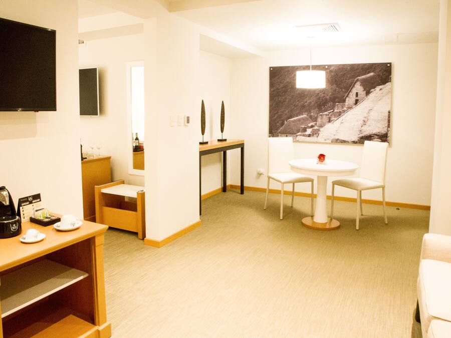 Ein Hotelzimmer mit Flachbildfernseher, einem kleinen Tisch mit Stühlen, einer Kaffeemaschine und einem großen gerahmten Bild an der Wand.