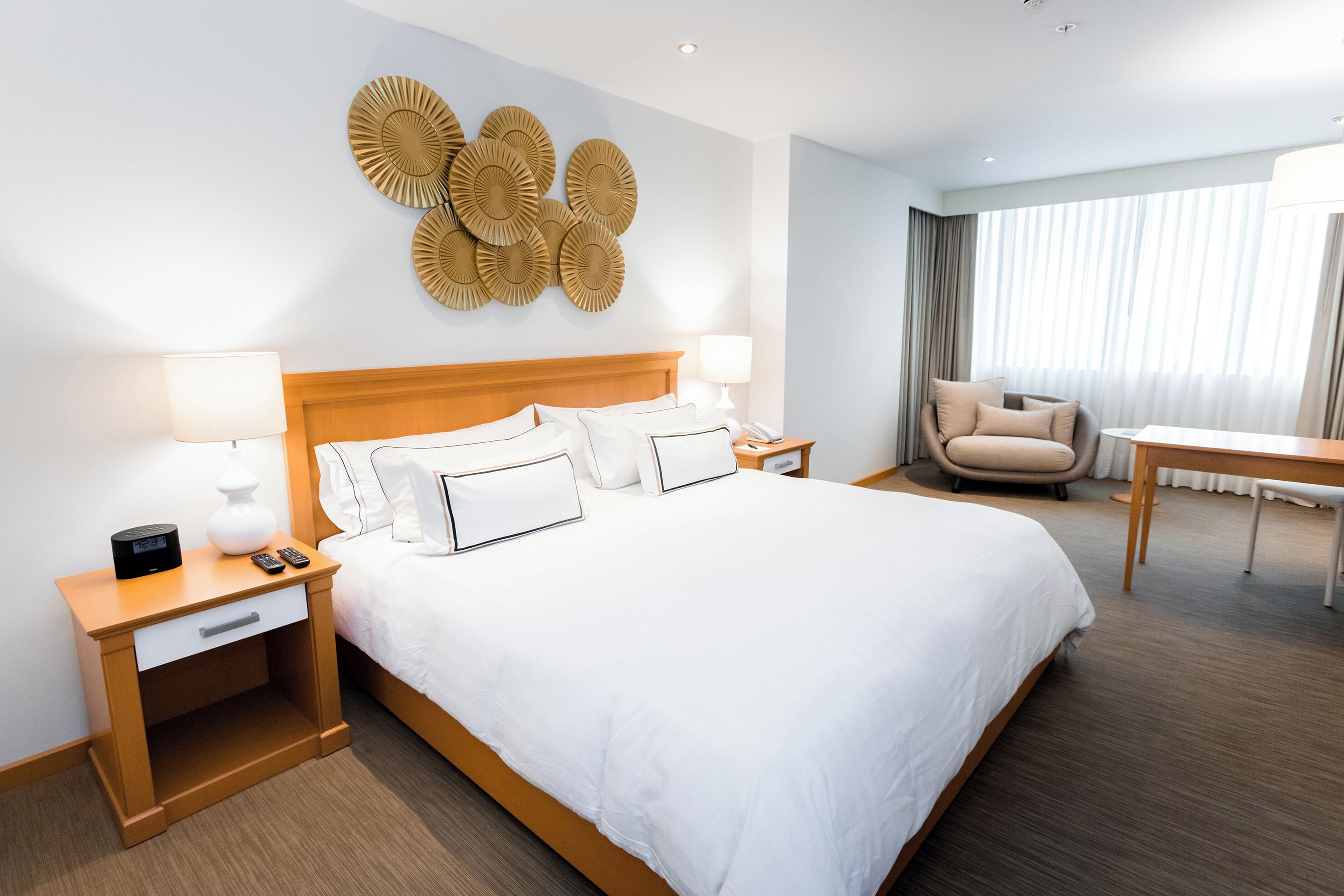 A hotel room with a large bed, bedside tables with lamps, a chair, a desk, and a wall art piece.