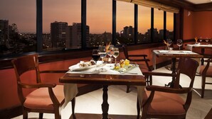 A dining area with a table set for two, featuring a city view at sunset. - Melia Lima (Lima)