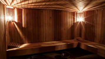 Una sauna de madera con bancos y un asiento de banco, y una pequeña mesa con un cuenco.