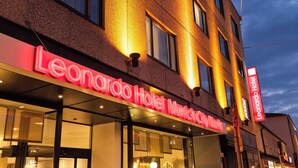 Das äußere Erscheinungsbild des Leonardo Hotels München CityCenter mit beleuchteter Beschilderung und einer modernen Fassade.