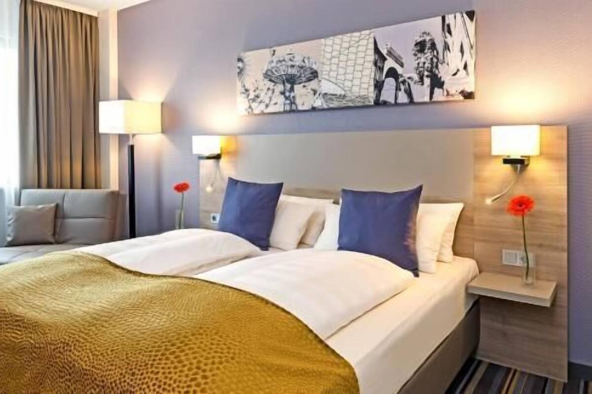 Een hotelkamer met een bed, twee nachtkastjes, een kunstwerk aan de muur en een lamp.